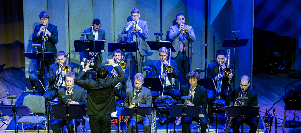 A group of musicians dressed in suits follow the director during a performance